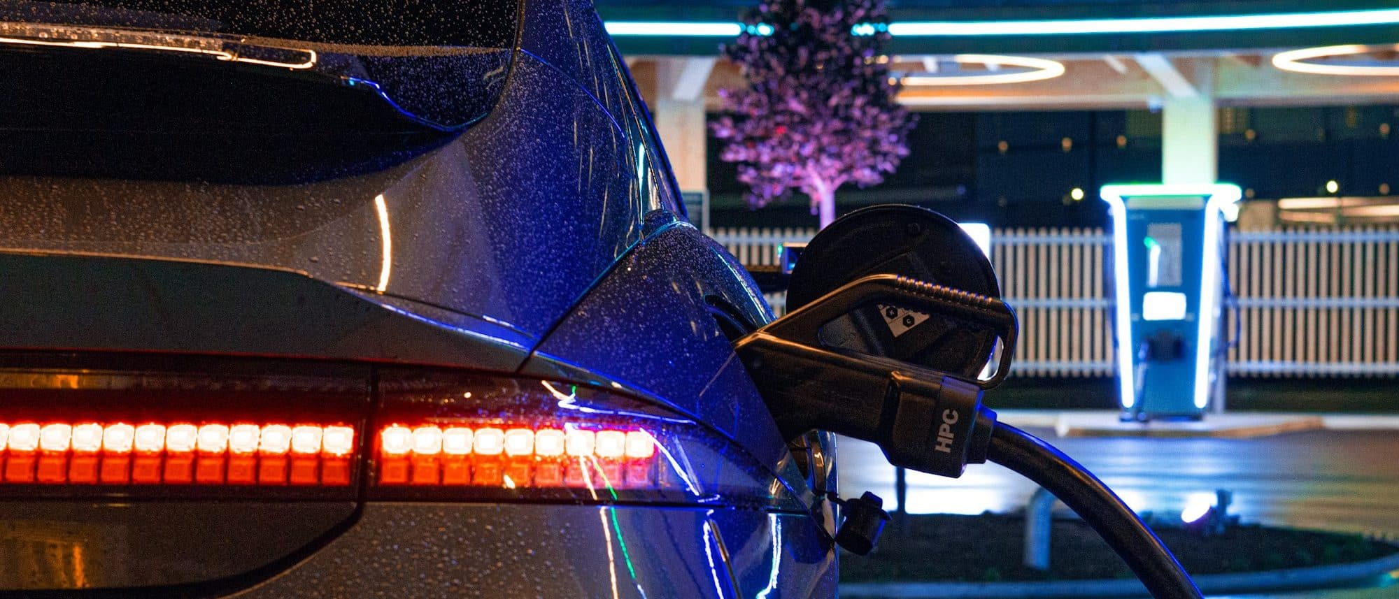 Electric vehicle charging at night, LED taillight strip and charge port in the rain