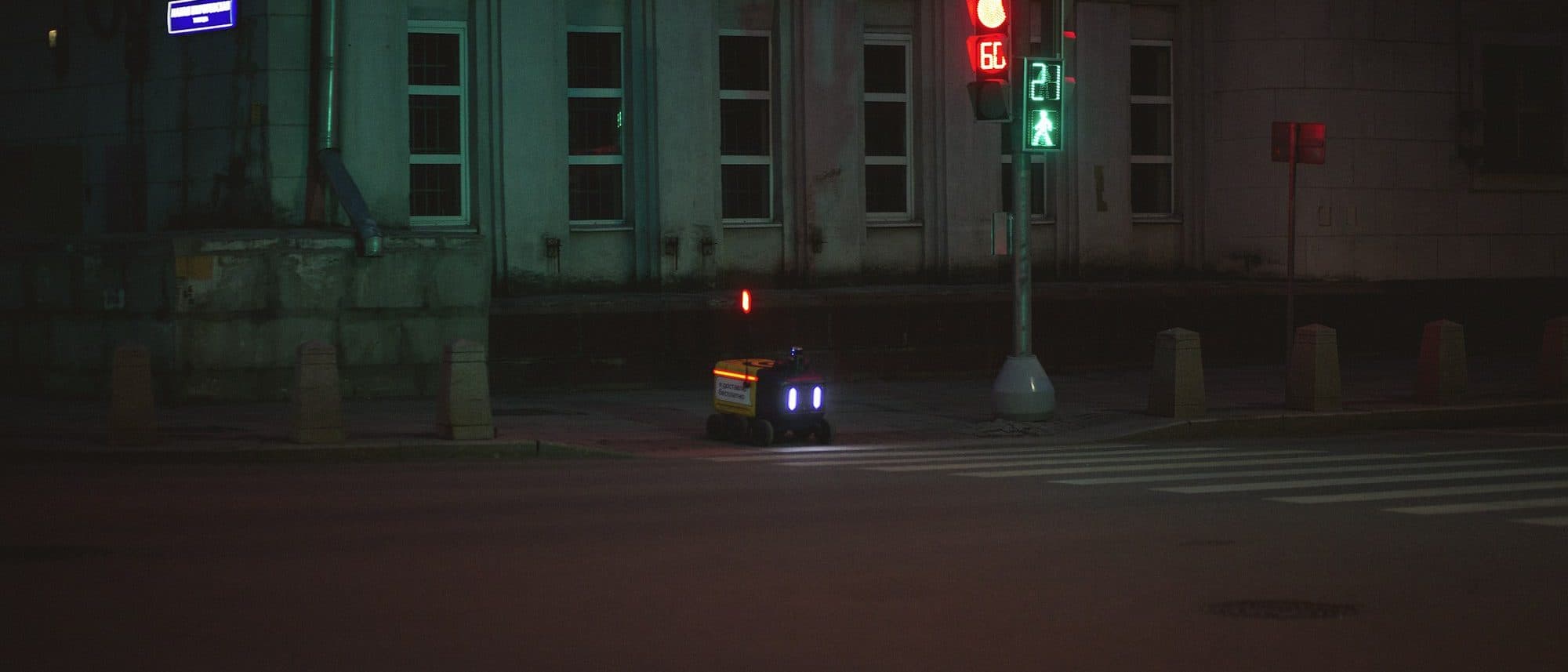 Delivery robot waiting alone at a night crosswalk under traffic lights