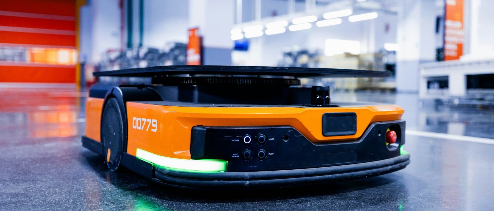 Autonomous mobile robot with green safety underglow on a polished warehouse floor
