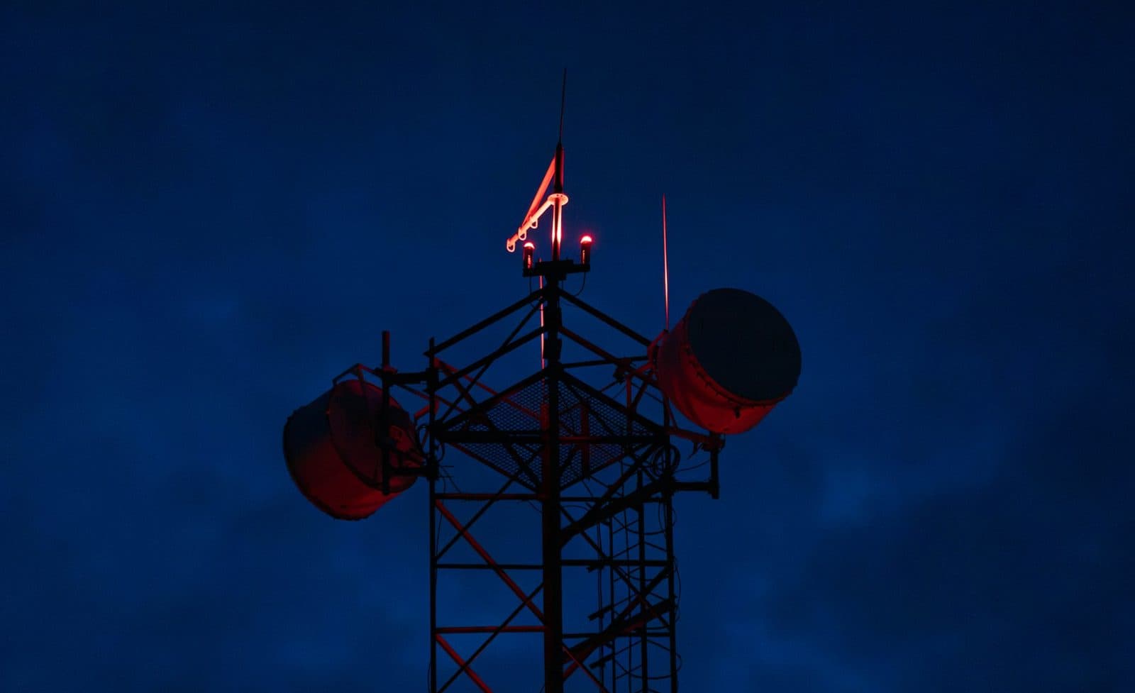 Microwave relay tower with red aviation lights against a dark night sky