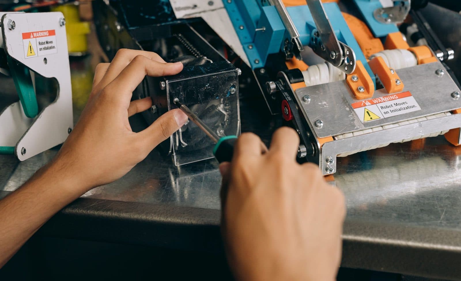 Engineer driving a screwdriver into a robot chassis on a steel workbench, warning labels on the frame