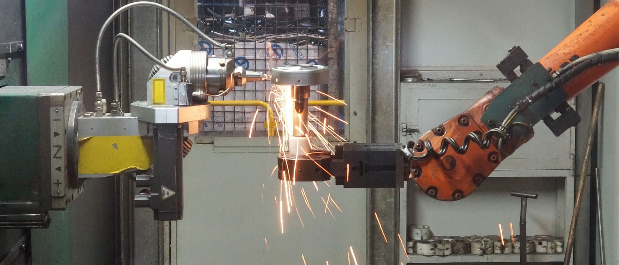 Industrial robot arm holding a part against a grinder with sparks flying on a shop floor